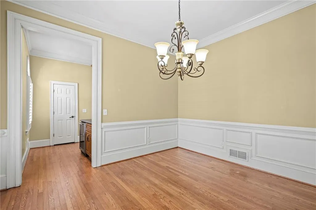 Unfurnished dining area featuring hanging lights, crown molding, light wood finished floors, a wainscoted wall, and a decorative wall