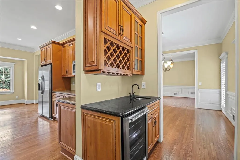 Bar featuring crown molding, wood finish cabinets, dark stone counters, wine cooler, and light wood-style flooring