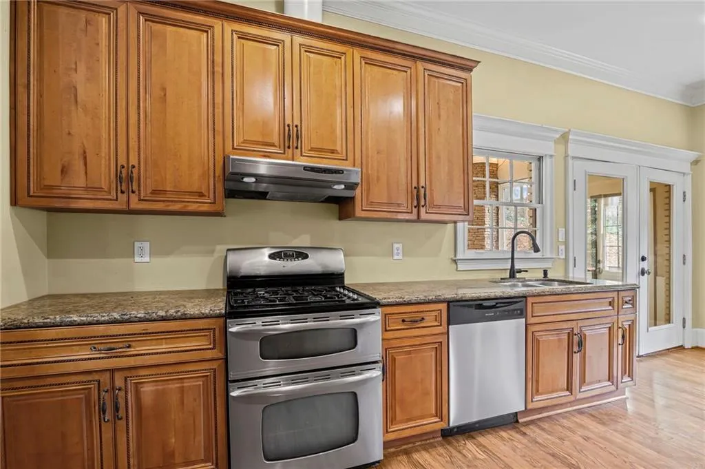 Kitchen featuring stainless steel appliances, wood finish cabinetry, crown molding, light wood-style flooring, and dark stone counters