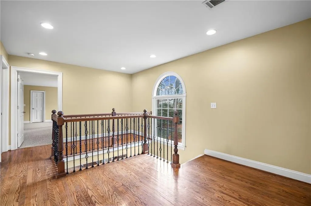 Corridor with an upstairs landing, wood finished floors, and recessed lighting