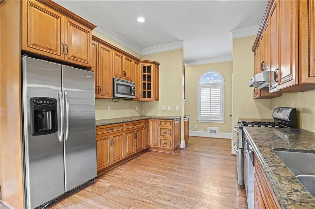 Kitchen with stainless steel appliances, dark stone counters, wood finish cabinets, glass insert cabinets, and light wood-style floors