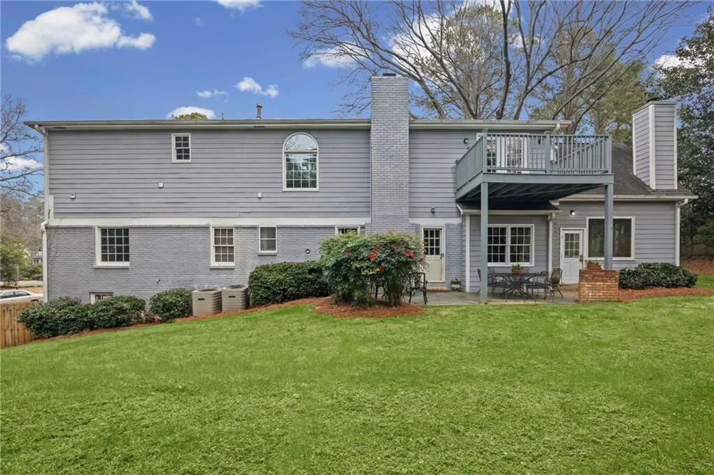 Rear view of house featuring a chimney, a patio, brick siding, and a lawn