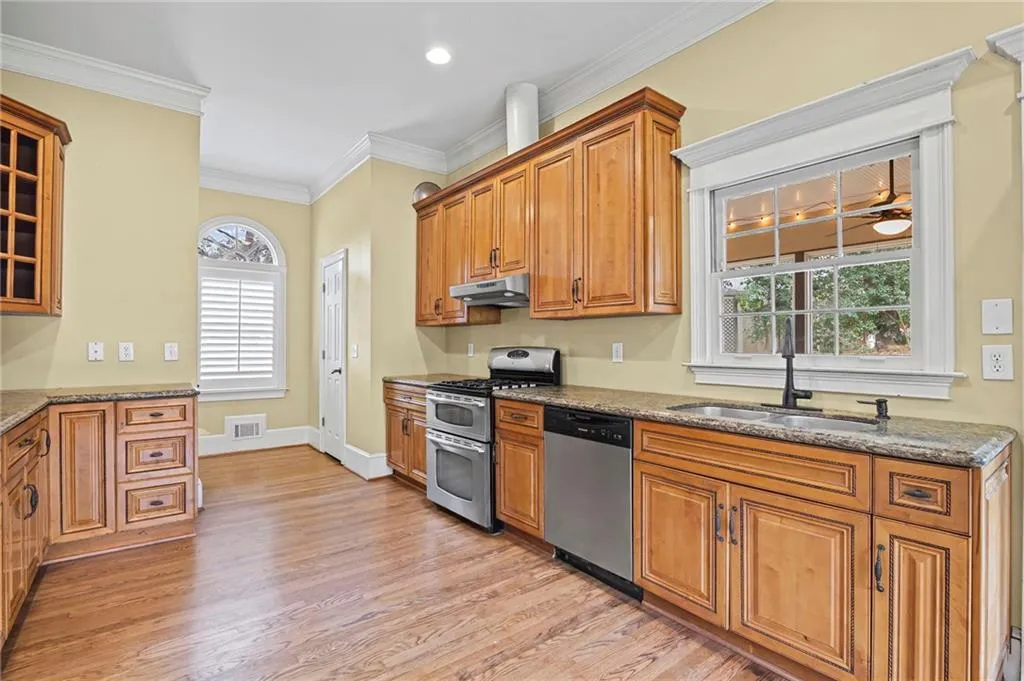 Kitchen with stainless steel appliances, wood finish cabinetry, light stone countertops, ornamental molding, and light wood-type flooring