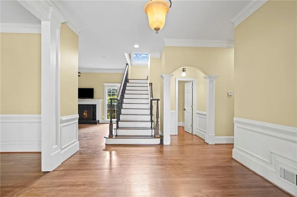 Entrance foyer featuring arched walkways, decorative columns, a warm lit fireplace, crown molding, and wood finished floors