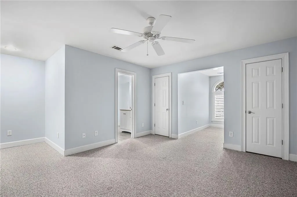 Unfurnished bedroom featuring light colored carpet, a ceiling fan, and multiple closets