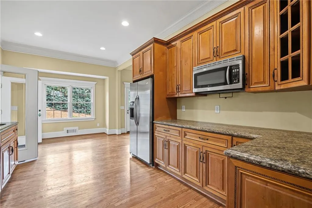 Kitchen featuring wood finish cabinetry, crown molding, dark stone counters, stainless steel appliances, and light wood-style flooring