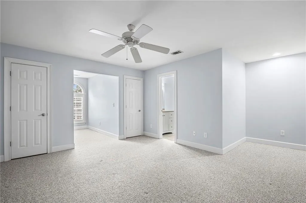 Unfurnished bedroom with light colored carpet, ceiling fan, connected bathroom, and multiple closets
