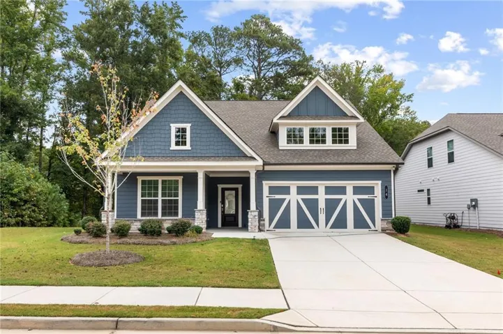 Traditional-style exterior with blue siding, stone column bases, a covered porch, a two-car garage, and a dormer window