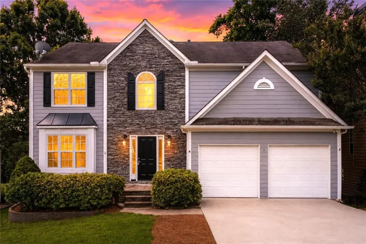 Two-story residence featuring a stone and siding facade, a two-car garage, manicured shrubbery, and a bay window