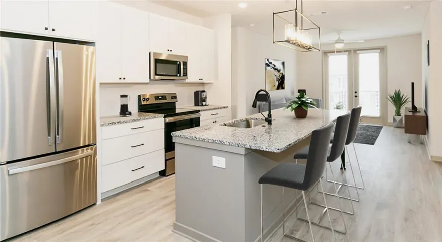 Kitchen with stainless steel appliances, an island with sink, light wood-style floors, a kitchen bar, and light stone countertops