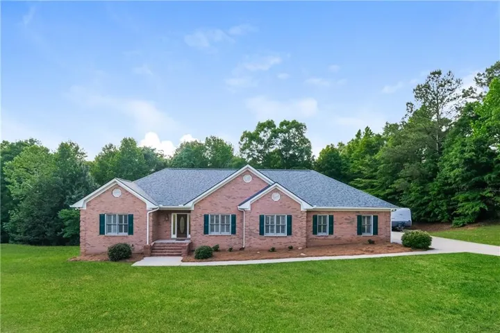Brick exterior residence featuring a gray shingle roof and dark green window shutters