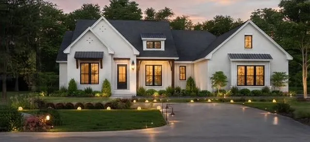 Modern farmhouse exterior featuring dark gabled roofs, contrasting white siding, black-framed windows, and a paved driveway with integrated ground lighting