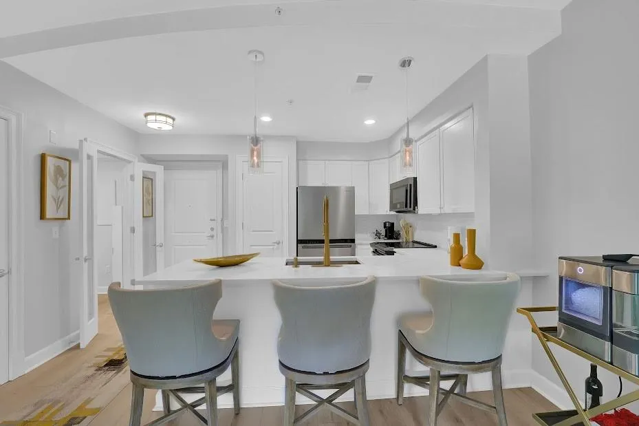 Kitchen featuring a kitchen bar, appliances with stainless steel finishes, light wood-type flooring, hanging light fixtures, and white cabinets
