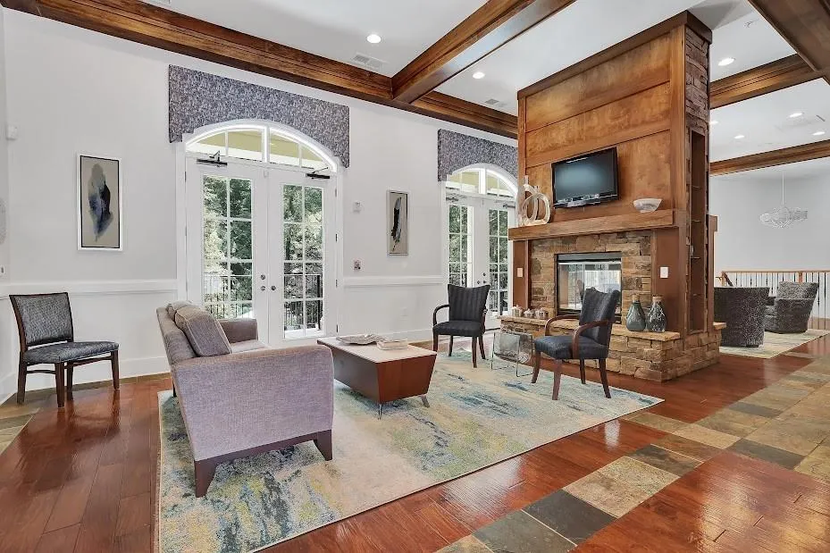 Living room with beamed ceiling, a notable chandelier, dark hardwood / wood-style floors, french doors, and a stone fireplace
