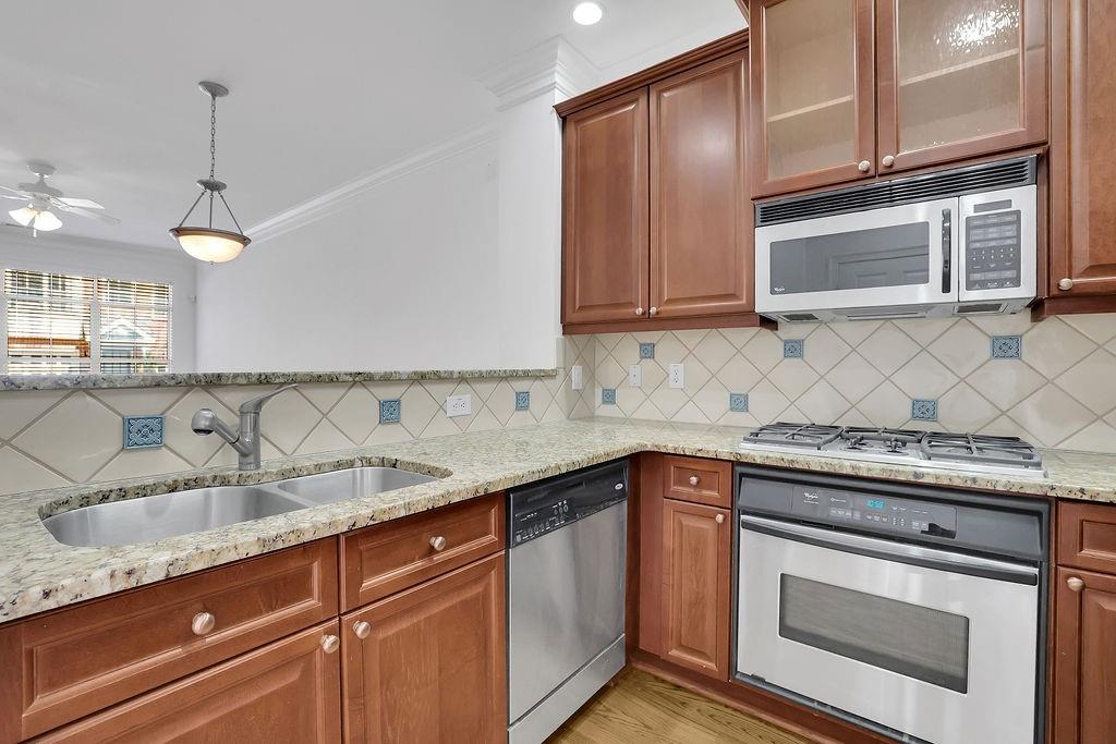 Kitchen with backsplash, light wood-type flooring, ceiling fan, light stone countertops, and appliances with stainless steel finishes