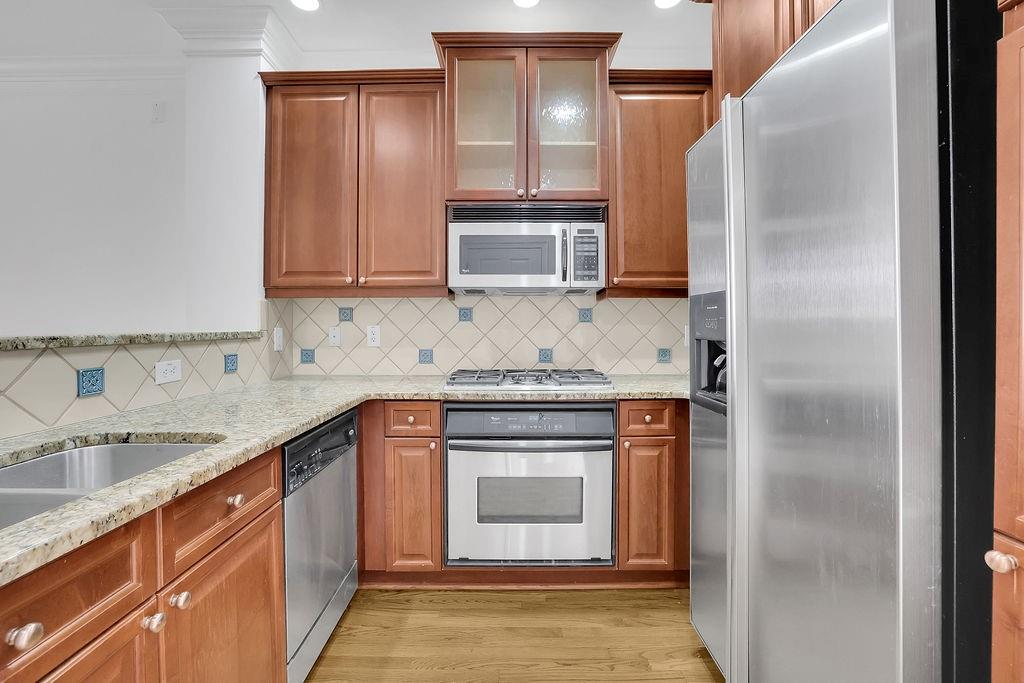 Kitchen with light stone counters, light wood-type flooring, ornamental molding, tasteful backsplash, and appliances with stainless steel finishes