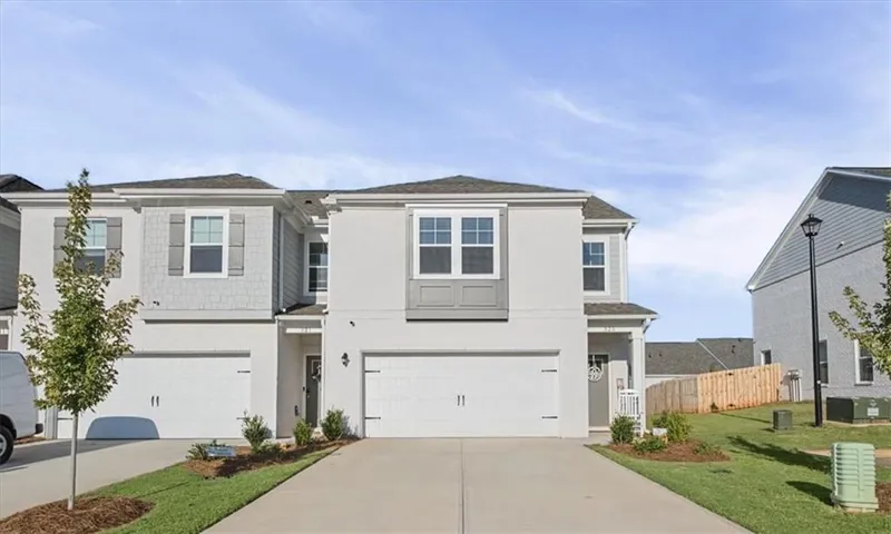 Two-story stucco and shingle exterior with multiple windows, attached garage, and landscaped front yard