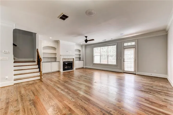 Spacious living area featuring wood-finish flooring, a fireplace with a mantel, built-in shelving, and a prominent window