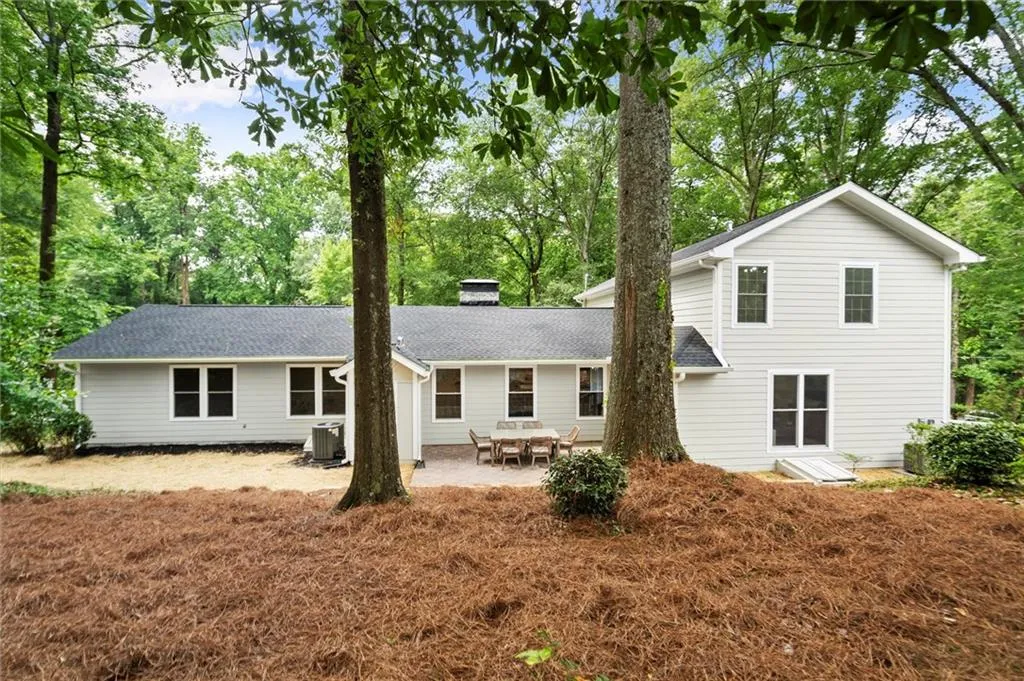 Rear view of house with a chimney, a patio, view of scattered trees, and roof with shingles