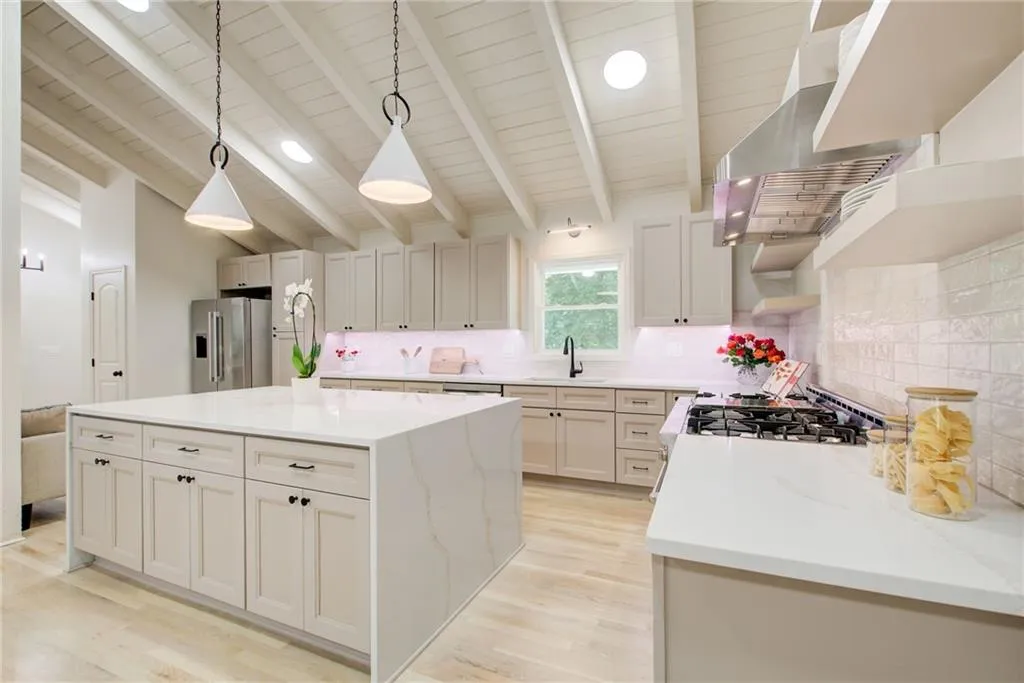 Take a look at this Chef's Kitchen featuring beautiful cabinetry, a  waterfall island, stainless steel appliances, vaulted ceiling, designer  backsplash, and pendant lighting