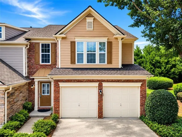 Brick and siding exterior with a two-car garage, mature landscaping, and an inviting entryway with a transom window