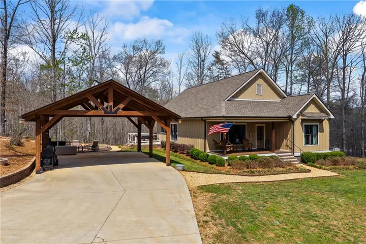 View of front of house with roof with shingles, a front lawn, concrete driveway, covered porch, and a detached carport