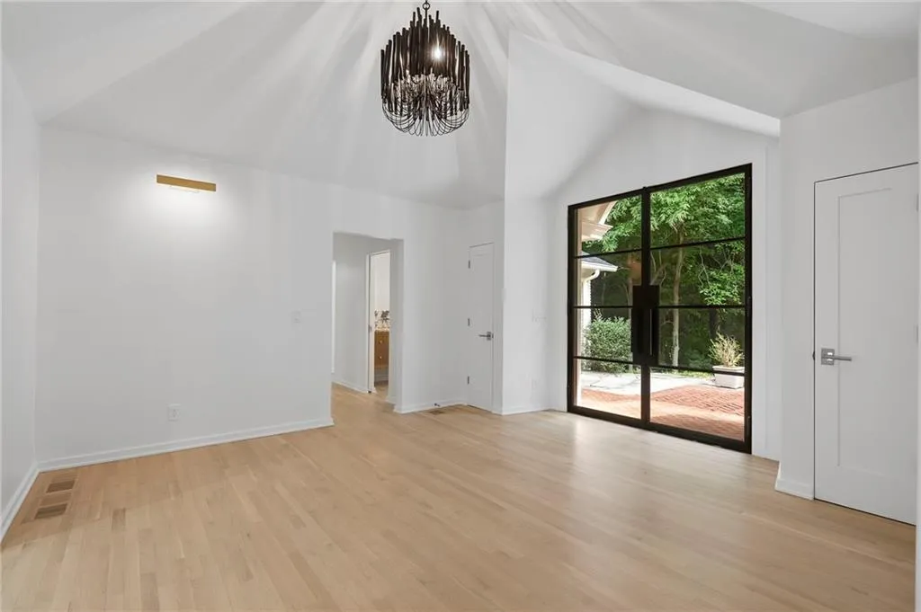 Vaulted ceiling with an ornate black chandelier, wood-finish flooring, and a large black-framed glass door opening to an outdoor patio area