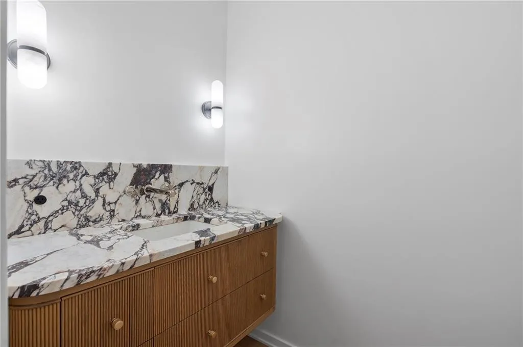 Custom vanity featuring a fluted wood-finish cabinet with brass hardware, a built-in rectangular sink, and a countertop and backsplash crafted from veined stone