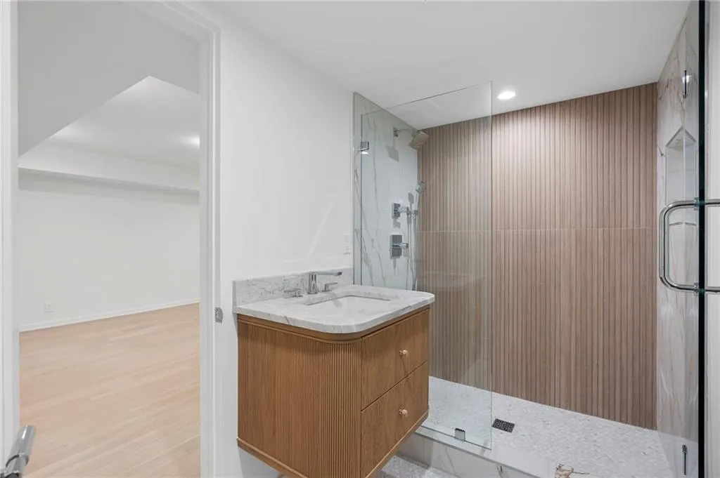 Contemporary bathroom featuring a floating wood-finish vanity with a stone countertop, a glass-enclosed shower with a rain showerhead, textured wall tiling, and recessed lighting