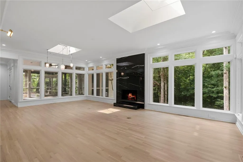 Expansive living area featuring light wood-finish flooring, a contemporary black marble-look fireplace, large windows, two skylights, and recessed lighting