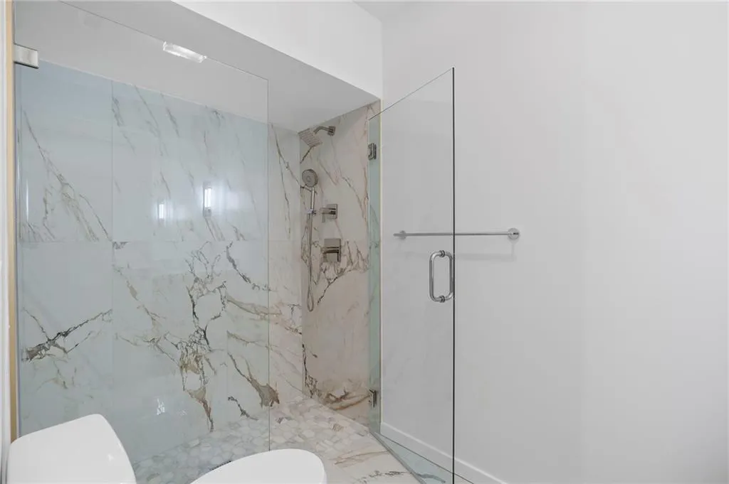 Modern walk-in shower featuring large format veined wall tiles, a rain shower head, and a separate handheld shower fixture