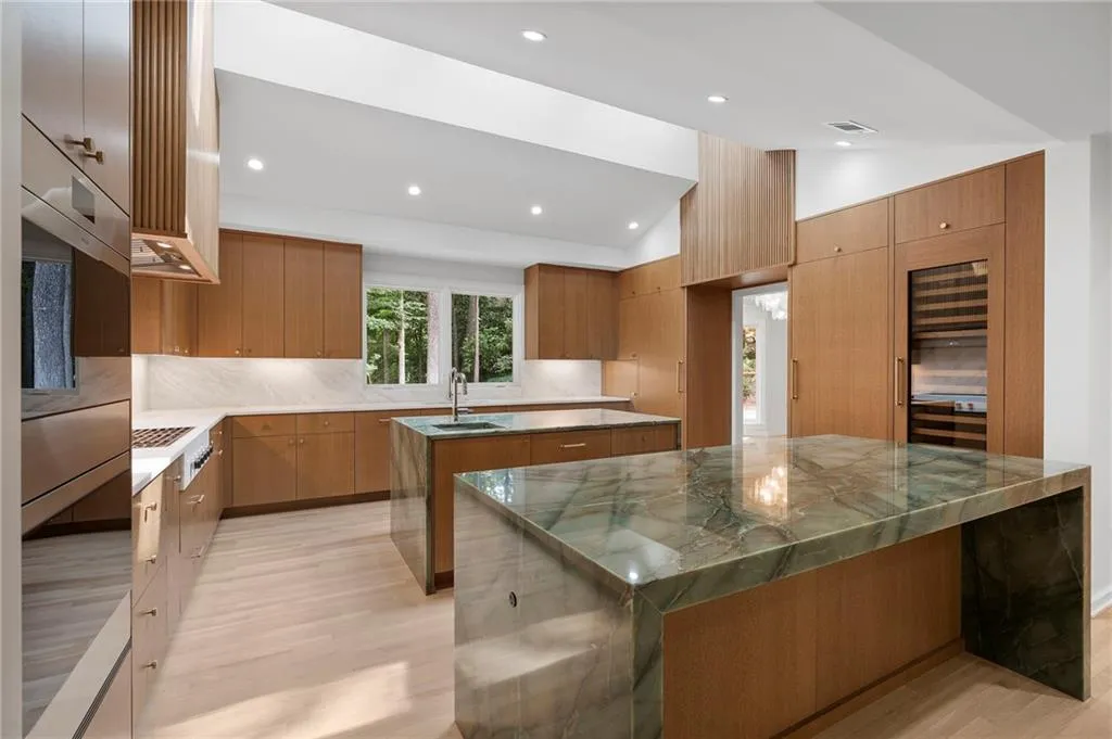 Contemporary kitchen featuring wood-finish cabinetry, light wood-finish flooring, and two waterfall-edge islands with stone countertops