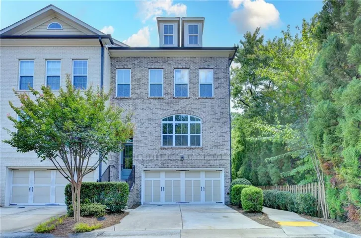 Brick facade townhome with arched window, dormer roof details, and an integrated two-car garage