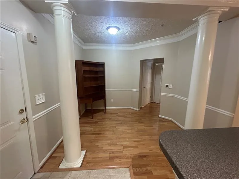 Hallway featuring a textured ceiling, ornate columns, light hardwood / wood-style flooring, and ornamental molding