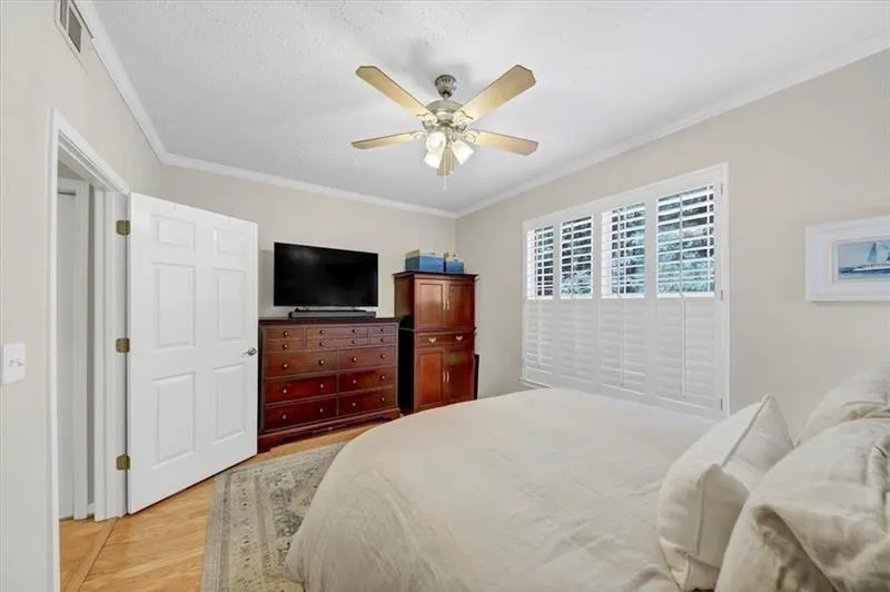 Bedroom featuring ceiling fan, a textured ceiling, light hardwood / wood-style flooring, and ornamental molding