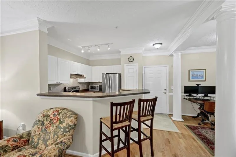 Kitchen with white cabinetry, kitchen peninsula, appliances with stainless steel finishes, ornate columns, and light wood-type flooring