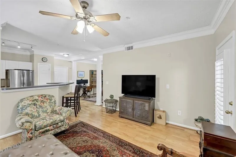 Living room with decorative columns, ceiling fan, light hardwood / wood-style flooring, and ornamental molding