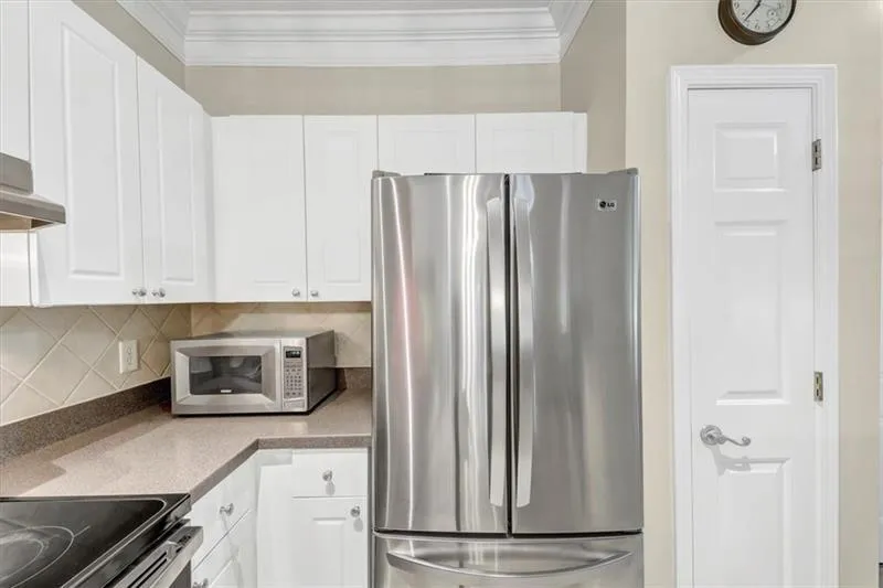 Kitchen with white cabinetry, appliances with stainless steel finishes, decorative backsplash, and ornamental molding