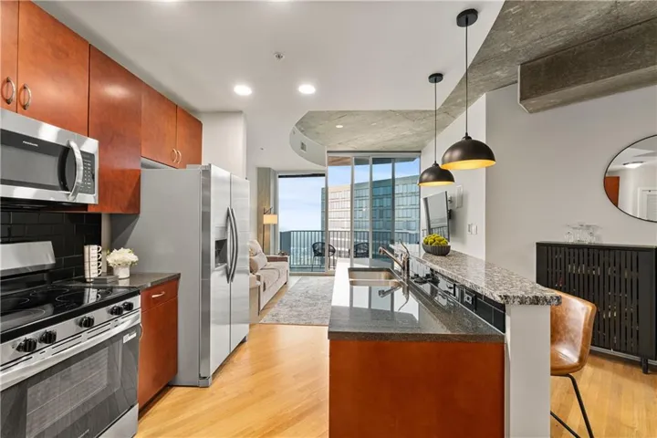Kitchen with stainless steel appliances, floor to ceiling windows, an island with sink, light wood-type flooring, and a breakfast bar