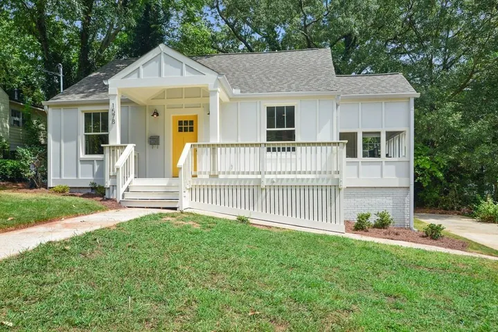 White exterior with vertical board and batten siding, yellow entry door, covered front porch, and an exterior deck with a ramp