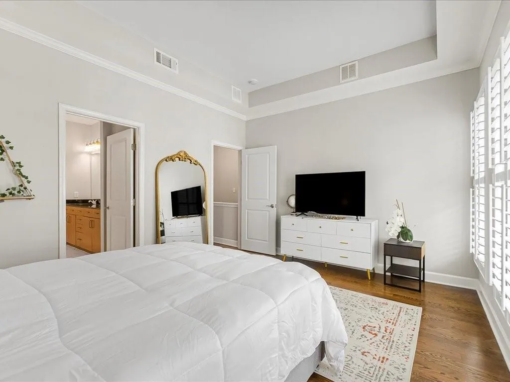 Bedroom featuring wood finished floors, crown molding, a tray ceiling, and ensuite bathroom
