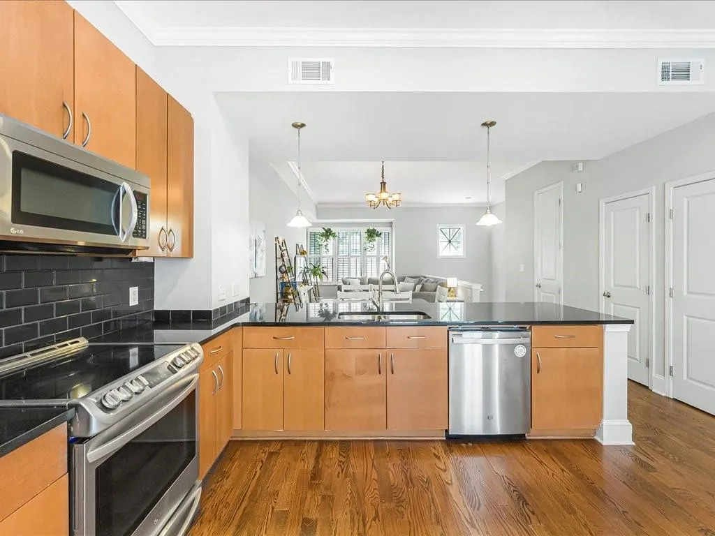 Kitchen with appliances with stainless steel finishes, ornamental molding, a peninsula, open floor plan, and dark wood-style floors