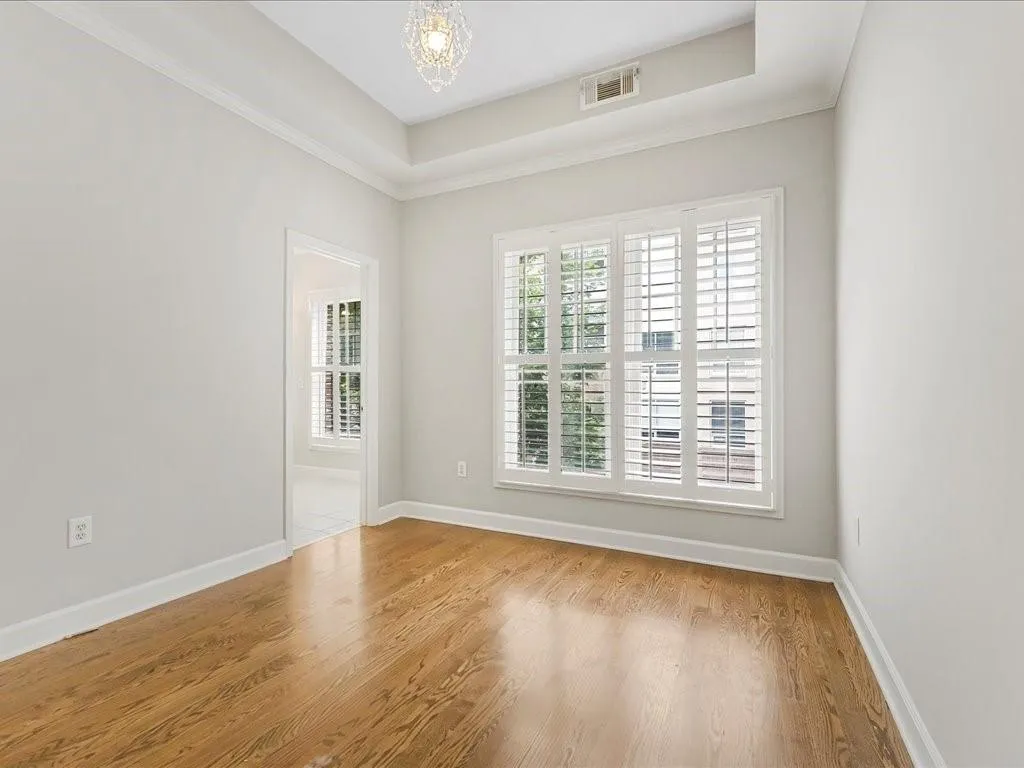 Unfurnished room with wood finished floors, a chandelier, a raised ceiling, and ornamental molding