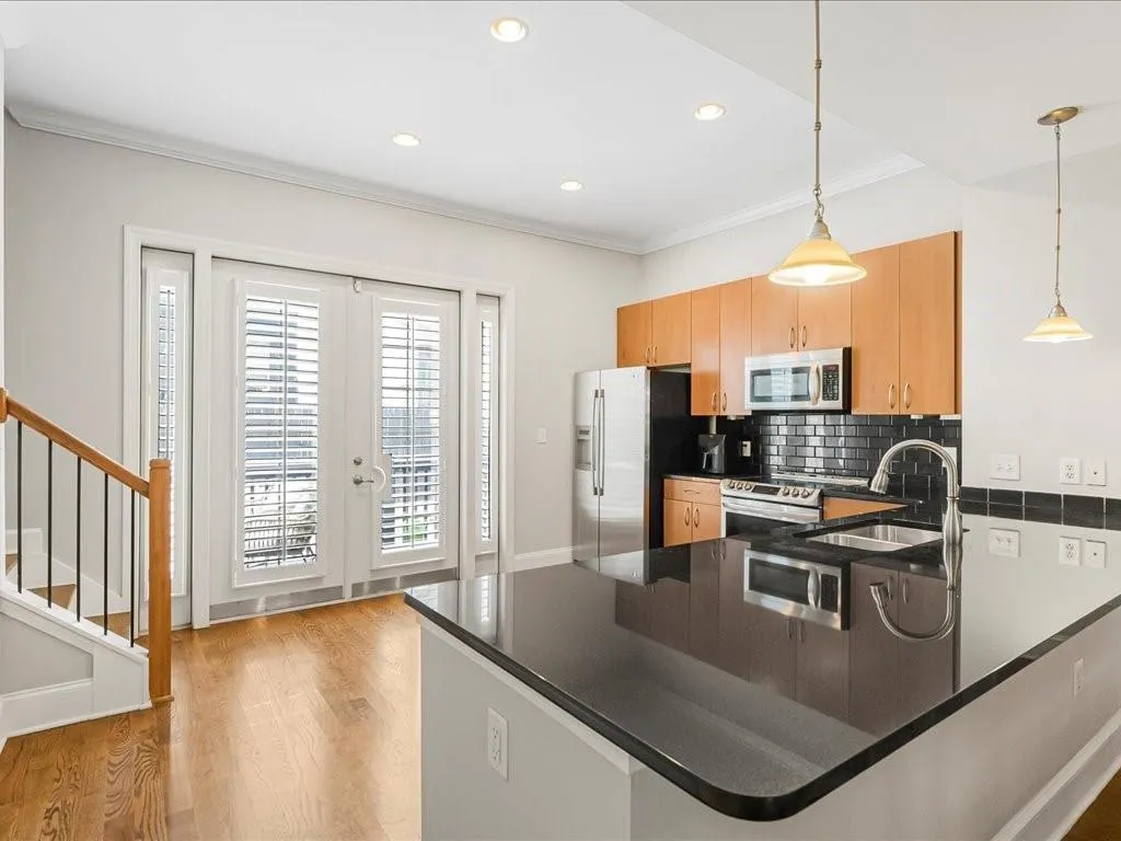 Kitchen with light wood-style floors, ornamental molding, stainless steel appliances, decorative backsplash, and a peninsula