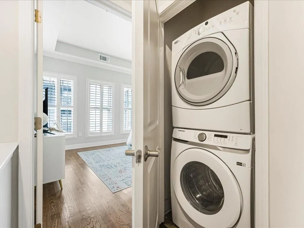 Washroom with stacked washer and clothes dryer and wood finished floors