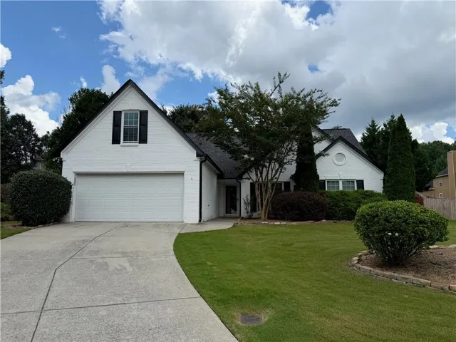 White brick exterior with a black shingle roof, attached garage, and a concrete driveway