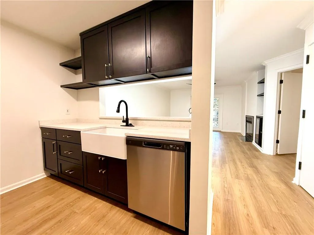 Kitchen featuring open shelves, stainless steel dishwasher, light wood-type flooring, light stone countertops, and a glass covered fireplace
