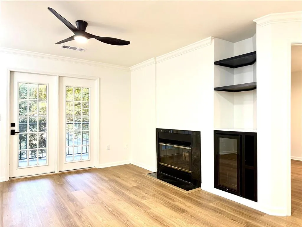 Unfurnished living room featuring light wood finished floors, ornamental molding, a fireplace with flush hearth, and ceiling fan