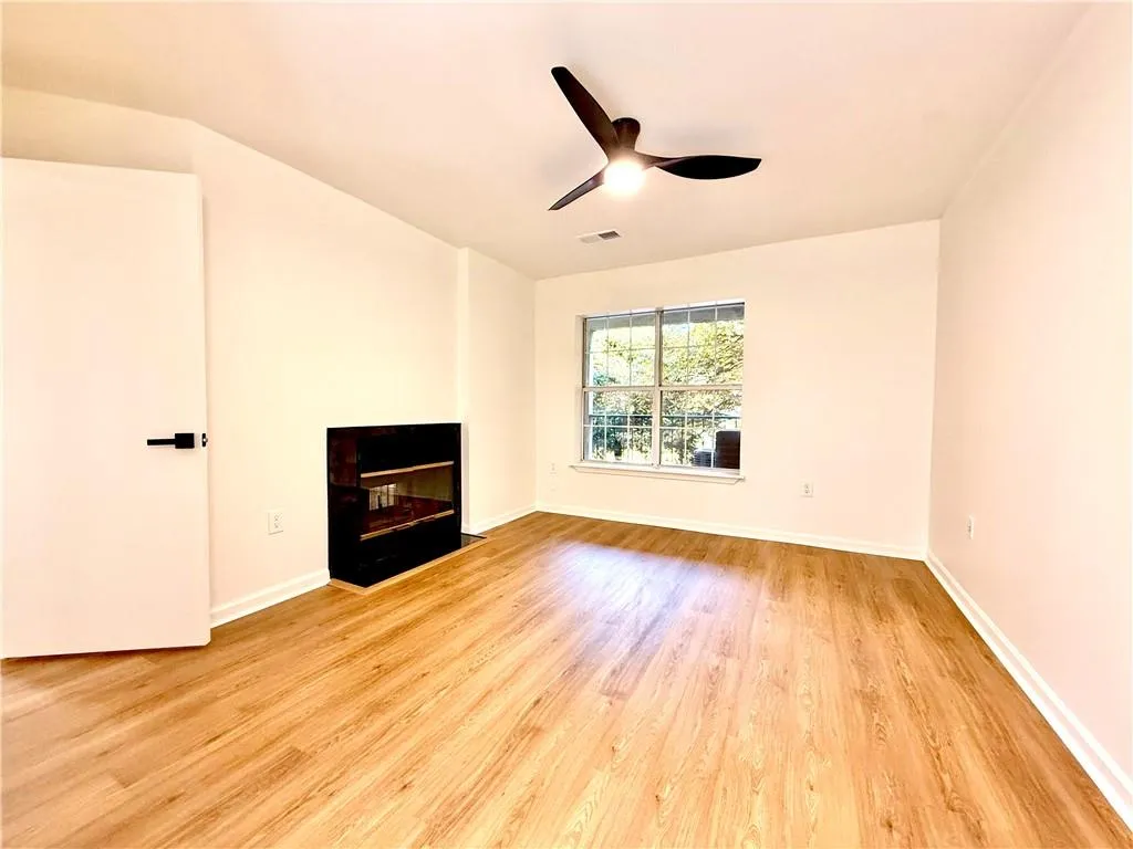 Unfurnished living room featuring a fireplace with flush hearth, light wood-type flooring, and ceiling fan