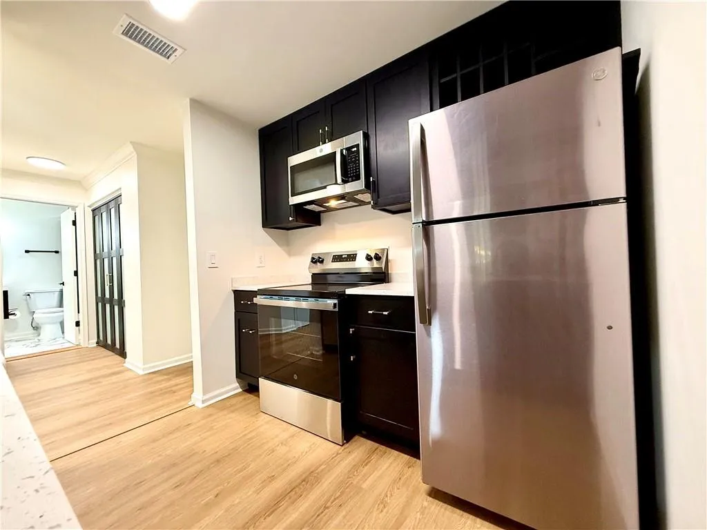 Kitchen with stainless steel appliances, dark cabinets, light countertops, and light wood-type flooring